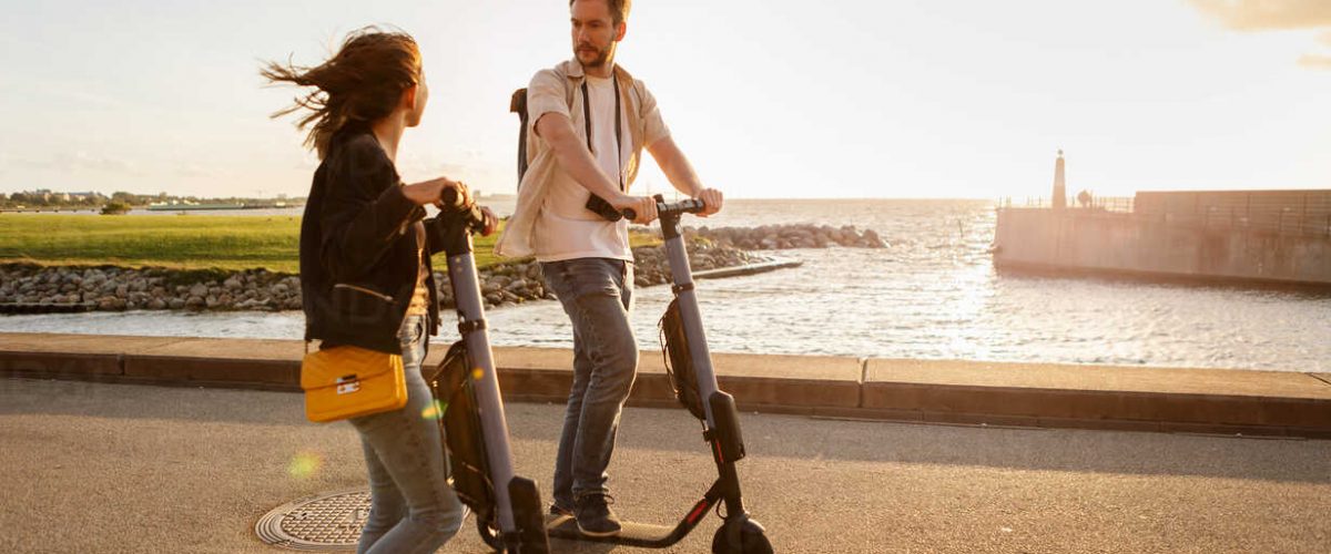 Couple talking while riding electric push scooters on road by sea against sky